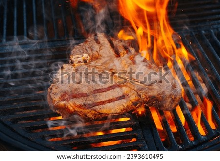 Barbecue dry aged wagyu porterhouse beef steak grilled as close-up on a charcoal grill with fire and smoke 