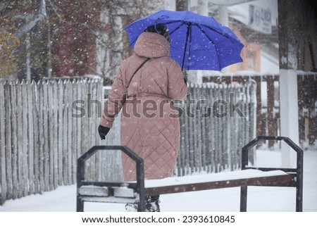 Yellow code and strong wind cyclone for a while in the winter. Picture of a grandmother holding a blue umbrella. Big flakes, winter, umbrella.
