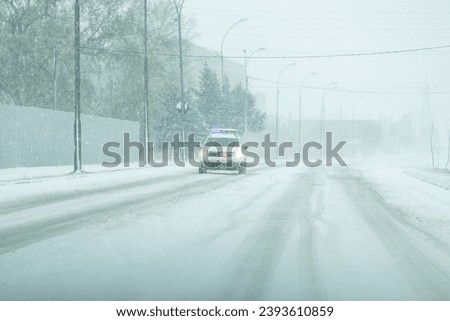 The picture of a police car that makes sure that everything is in order and that the drivers take care of the traffic rules because outside there is a yellow code for strong wind and snow.