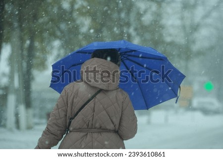 The picture of a grandmother holding a blue umbrella on a background of the winter season. The umbrella serves as a shelter for the snowflakes.