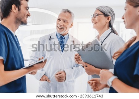 Multiracial team of doctors discussing patient standing in clinic foyer, learning new about illnesses, medical cases, diseases. Treatment and recuperation. Healthcare Royalty-Free Stock Photo #2393611743
