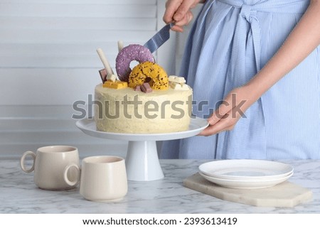 Woman cutting delicious cake decorated with sweets at white marble table, closeup Royalty-Free Stock Photo #2393613419