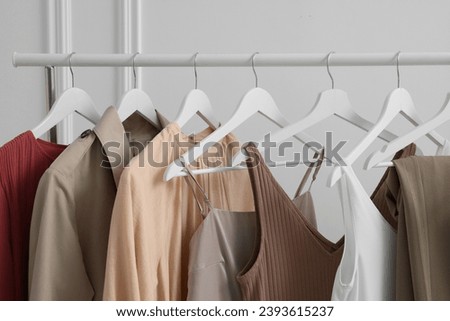 Rack with different stylish women`s clothes near white wall indoors, closeup Royalty-Free Stock Photo #2393615237