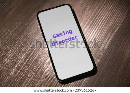 Smartphone with phrase Gaming Disorder on wooden table, closeup. Addictive behavior