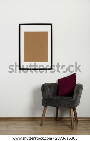Comfortable armchair, cushion and picture frame on wall indoors. Interior element