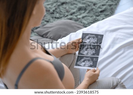 Pregnant woman looking at ultrasound scan of baby, close up of scan. X-ray image photo of fetus embryo. Expectant mother checking on medical document Royalty-Free Stock Photo #2393618575