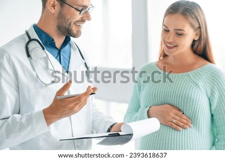 Close up shot of male doctor showing prescription document to pregnant woman in clinic. Medications for expectant mother, natality and fertility concept Royalty-Free Stock Photo #2393618637