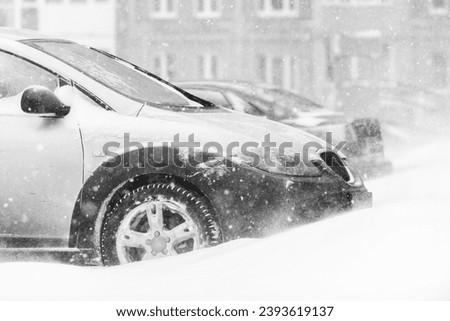 Snow storm, snow-covered street and a car in a snowdrift covered with snow in winter. Blizzard - automobile traffic in bad weather conditions Royalty-Free Stock Photo #2393619137