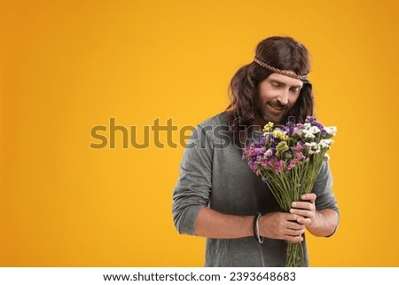 Hippie man with bouquet of colorful flowers on orange background, space for text