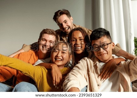 multiracial group of young friends smiling and taking selfies for the camera, asian, african american and european students hugging and taking pictures together