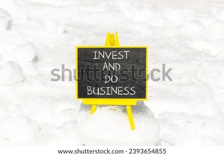 Invest and do business symbol. Concept word Invest and do business on beautiful black chalk blackboard. Beautiful white snow background. Invest and do business concept. Copy space.