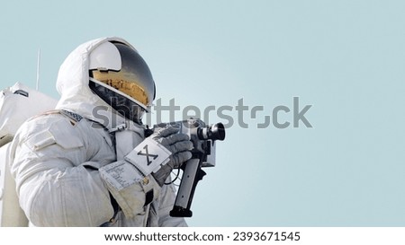 Space man photographer astronaut in a space suit with a helmet holds a photo camera and takes pictures on a blue background. Production photo and video concent, creative idea. Video recording, concept