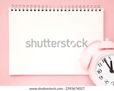 Pink background with empty blank notebook paper and alarm clock at 1 o clock