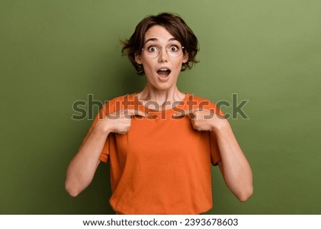 Photo of excited impressed young woman dressed orange t shirt open mouth pointing fingers herself isolated on green color background