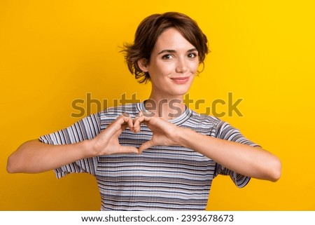 Portrait of appreciative girl with short hairstyle wear grey t-shirt fingers showing heart symbol isolated on yellow color background