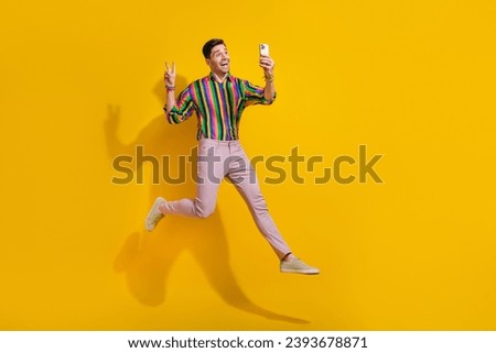 Full size photo of young guy trampoline jumper show v sign at party hipsters striped shirt make selfie isolated on yellow color background