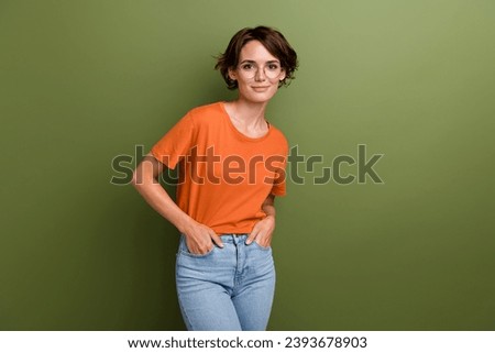 Photo of clever adorable cheerful girl with bob hairdo dressed orange t-shirt hold palms in pockets isolated on khaki color background
