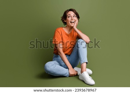 Full size photo of impressed woman dressed orange t-shirt jeans in glasses sit look at sale empty space isolated on khaki color background