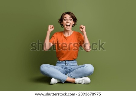 Full size photo of ecstatic funny woman wear t-shirt in glasses sit on floor clenching fists win bet isolated on khaki color background Royalty-Free Stock Photo #2393678975