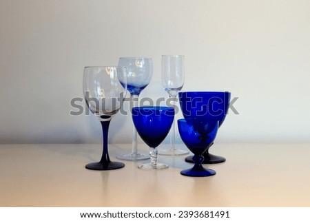 Series of blue stemmed glasses in different shapes and sizes set in soft light on plain cream background