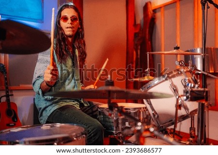 Talented and stylish young male drummer playing drums with drum sticks, looking at a cymbal in a music studio. He looks focused and improvising while performing. A drummer is playing his instrument. Royalty-Free Stock Photo #2393686577