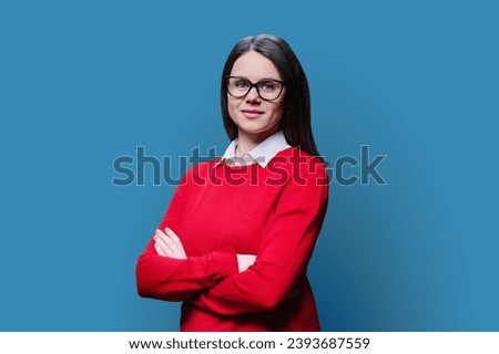 Young smiling woman with crossed arms looking at camera on blue background
