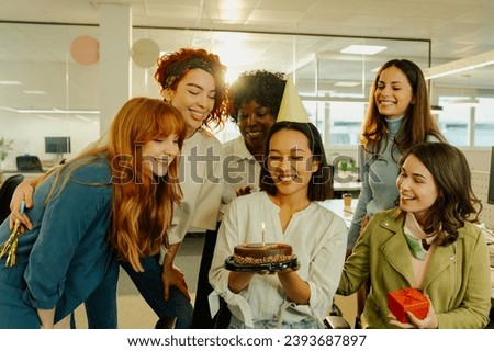 A multicultural diverse female colleagues having birthday party at office. A japanese businesswoman is holding a birthday cake while her friends are gathered around her and celebrating with her.