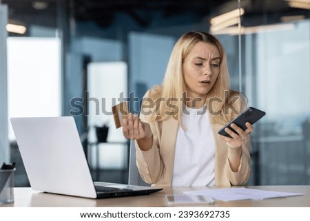 Frustrated sad upset woman working inside office, cheated business woman refused online money transfer, female worker displeased holding bank credit card and phone. Royalty-Free Stock Photo #2393692735