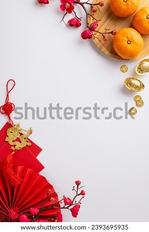 Embrace Chinese New Year atmosphere with top view vertical image of lively fan, ancient coins, sycee, envelopes, dragon charm hanging, plate of tangerines, sakura on white background, space for text