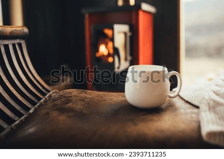 White cup with hot tea with burning fireplace on the background in cozy log cabin. Royalty-Free Stock Photo #2393711235