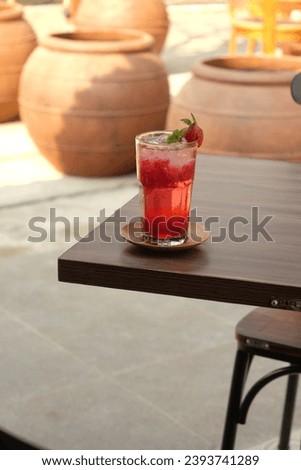 A refreshing strawberry mocktail on a wooden table, in a relaxed outdoor cafe setting, garnished with a fresh strawberry and mint.