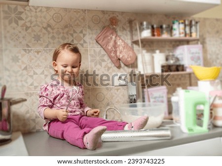 Little girl sitting on kitchen counter and helps her mommy make cookies  Royalty-Free Stock Photo #2393743225