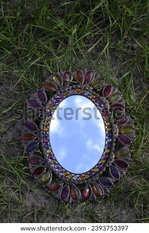 A photograph of a mirror laying in the grass with the sky reflecting in the image area of the mirror. 
