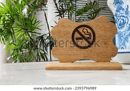 Do not smoke sign. Wooden signboard on blurred nature background.  A brown wooden sign placed on a wooden table inside the park reads NO SMOKING in dark brown. 