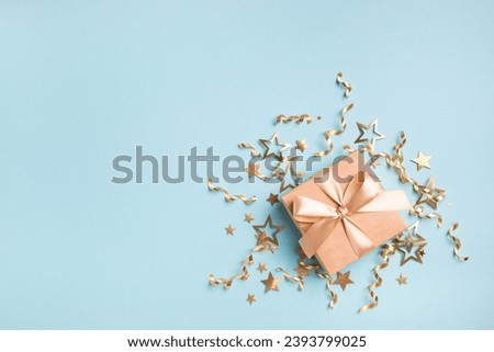 Christmas or birthday card with gift or present box and golden decorations from stars and confetti on blue turquoise background. 