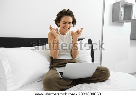 Portrait of woman in bedroom, sitting on bed, using laptop, waiting for good news, praying, making wish, anticipating something, waiting for positive outcome with crossed fingers.
