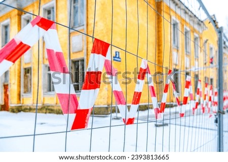 Red and white lines of barrier tape on the entrance gate in selective focus. Striped red and white tape prohibiting access to a construction site. Protection against entry into the territory. Royalty-Free Stock Photo #2393813665