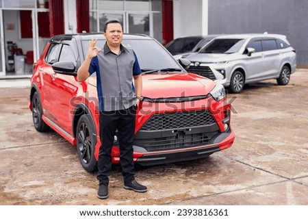 Young handsome smiling Asian man getting a new car and showing okay sign. Buy or rent a car concept