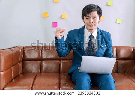 Satisfied asian businessman showing snap finger get idea with laptop sitting on sofa at home. Success cheerful positive young man wear suit use laptop work online holding snap finger at workplace. Royalty-Free Stock Photo #2393834503