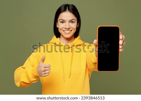 Young fun Latin woman she wears yellow hoody casual clothes hold in hand use mobile cell phone with blank screen workspace area show thumb up isolated on plain pastel green background studio portrait