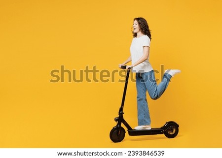 Side profile view young European woman she wear white blank t-shirt casual clothes driving electric scooter look camera isolated on plain yellow orange background studio portrait. Lifestyle concept
