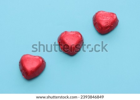 Three heart-shaped chocolates wrapped in red foil, top view.