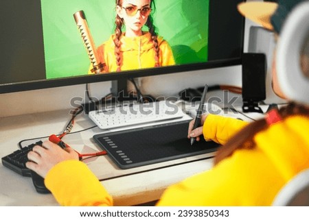 A young girl draws on a PC using a graphics tablet in comfortable home office. Close-up of hand with a pencil stilus.