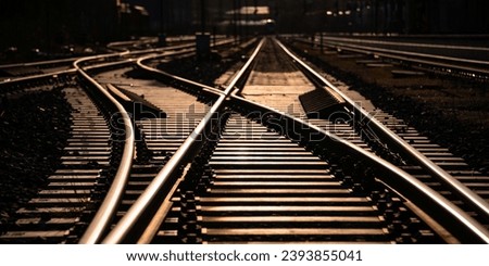 Railway track panorama and switches at station in Sauerland Germany with geometrical structure and vanishing point. Warm evening sunlight reflected by bright steel surface, screws and thresholds. Royalty-Free Stock Photo #2393855041