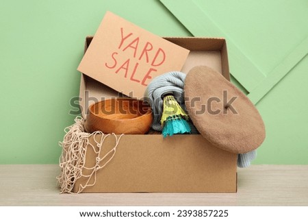 Box of unwanted stuff and cardboard sign with text YARD SALE on green background