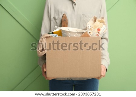 Woman holding box of unwanted stuff for yard sale on green background Royalty-Free Stock Photo #2393857231