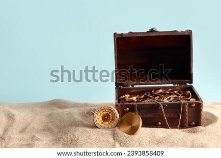 Old chest with treasures and compass on sand against blue background