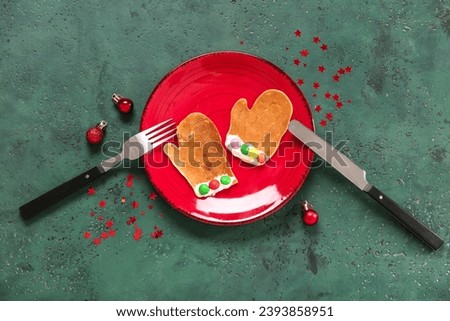 Plate with pancake in shape of mittens on green table. Christmas celebration