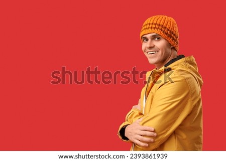 Young man in stylish jacket and hat on red background
