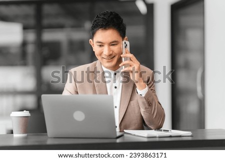 Asian professional male business person in beige suit and white shirt is working on laptop and holding pen, looking focused.